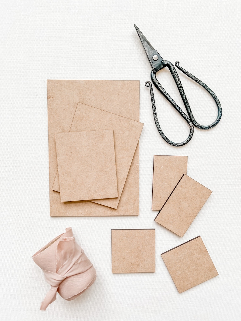 May include: A set of six brown cardboard squares of varying sizes, a pair of black metal scissors, and a roll of pink fabric ribbon.