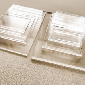 May include: Two stacks of clear acrylic squares of varying sizes. The squares are stacked on top of each other, creating a tiered effect.
