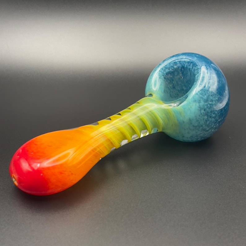 Op de afbeelding: Een kleurrijke glazen pijp met een kom en steel. De kom is blauw, verloopt naar turquoise, dan geel en oranje op de steel, eindigend in rood. De pijp heeft een gladde, glanzende afwerking.