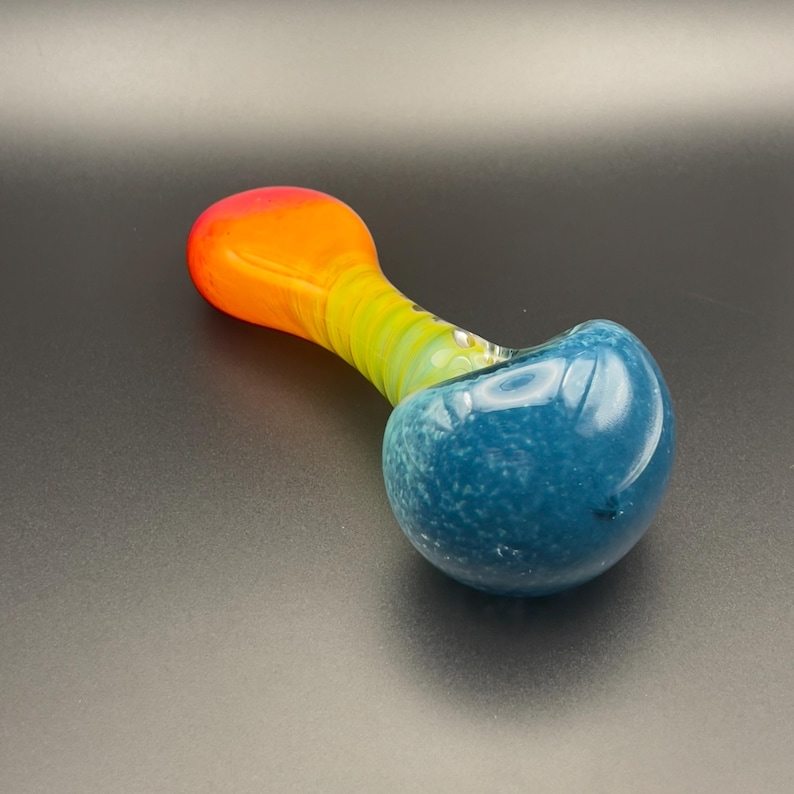 Op de afbeelding: Een kleurrijke glazen pijp met een afgeronde blauwe kom en een steel die overloopt van geel naar oranje. De pijp is ontworpen met een gladde, glanzende afwerking.