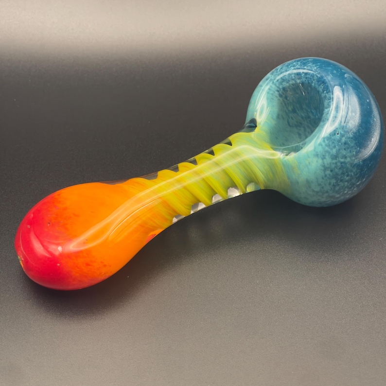 Op de afbeelding: Een kleurrijke glazen pijp met een kom en een steel. De kom heeft een verloop van blauw en turquoise, overgaand in geel en oranje op de steel. Het uiteinde van de steel is rood.