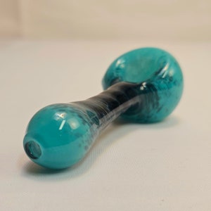 May include: A teal and black glass pipe with a rounded bowl and mouthpiece. The stem is black with teal marbling. The pipe is designed with a smooth, ergonomic shape.