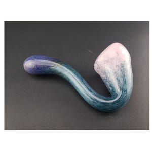 May include: A hand-blown glass pipe with a curved design. The pipe features a color gradient, transitioning from a pink bowl to a blue and teal stem. The glass has a marbled appearance, with streaks of color throughout.