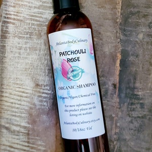 May include: A brown glass bottle of Patchouli Rose Organic Shampoo. The label is white with blue and pink watercolor floral designs. The label reads "Atlanta Body Culinary", "Patchouli Rose", "100% Organic", "Organic Shampoo", "Organic/Vegan/Chemical Free", "For more information on this product please see the listing on website AtlantaBodyCulinary.etsy.com", and "10/18oz Vol".