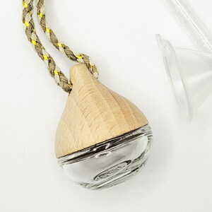May include: A teardrop-shaped glass and wood essential oil diffuser with a braided tan, yellow, and brown cord. The diffuser has a clear glass base and a light-colored wooden top. A clear plastic piece is visible in the background.