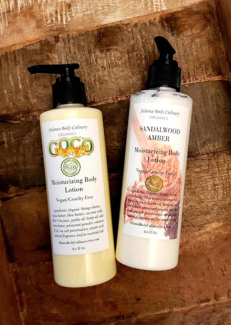 May include: Two 8.6 fl oz bottles of organic body lotion. The bottle on the left is labeled "Coco Mango!" and the bottle on the right is labeled "Sandalwood Amber". Both bottles are white with black pump tops and feature a label with the company name "Atlanta Body Culinary Organics".