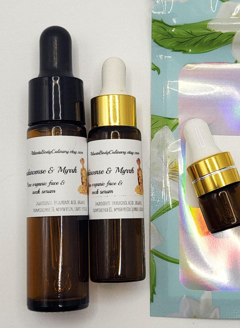 May include: Two amber glass bottles of face and neck serum with black and gold droppers. The labels read "Frankincense & Myrrh" and list ingredients. A small bottle with a white dropper is also visible.