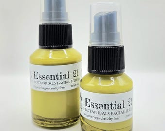 May include: Two clear glass bottles filled with a yellow facial serum, each topped with a black pump dispenser and a clear cap. The white labels read Essential 21 Botanicals Facial Serum, Organic/vegan/cruelty free, and .075/1.4oz.