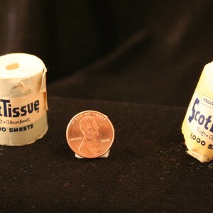 May include: Two miniature rolls of ScotTissue, one blue and one yellow, each with the text "ScotTissue Soft Absorbent 1000 Sheets". A US penny is in the center of the image for scale.