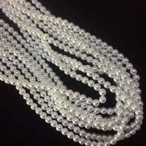 May include: A strand of white faux pearl beads, arranged in a layered pattern, against a black background.