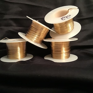 May include: Four spools of gold wire on white plastic spools. The spools are stacked on top of each other. The wire is wound tightly around the spools. The spools are labeled with the letter "ee".