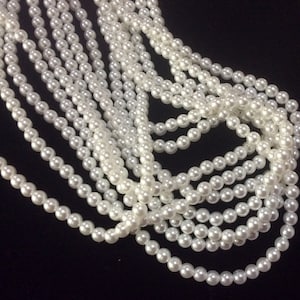 May include: A strand of white faux pearl beads, arranged in a loose pile on a black background.