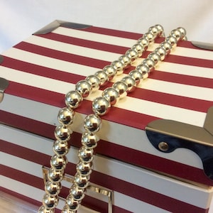 May include: A red and white striped box with gold accents and a gold beaded necklace draped over it.