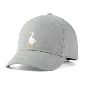 May include: A light gray baseball cap featuring an embroidered white goose with yellow feet. The cap has a curved brim and a button on top. The hat is made of a soft material and is suitable for casual wear.