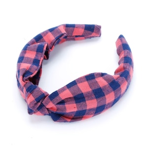 May include: A pink and blue plaid knotted headband. The headband is made of a soft, stretchy fabric and is perfect for adding a touch of style to any outfit.