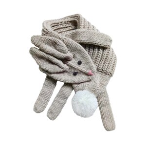 May include: A beige knitted scarf and gloves set with a bunny rabbit design. The gloves have a white pom-pom on the end and black eyes and a pink nose.