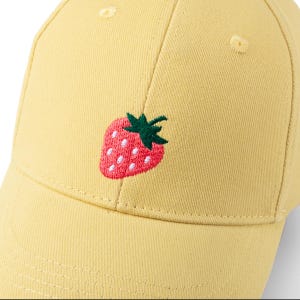 May include: A yellow baseball cap with a red and green embroidered strawberry on the front.