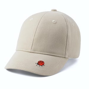 Puede incluir: Una gorra de béisbol beige con una pequeña mariquita roja bordada en la parte delantera.