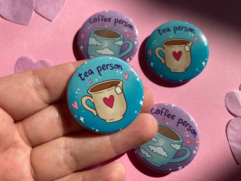 May include: Four circular badges with coffee and tea cup designs. Two badges say "coffee person" and show a cup with clouds. Two badges say "tea person" and show a cup with a heart. The background is pink.