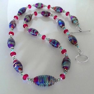 May include: A long necklace with colorful, swirled glass beads and silver accents. The beads are oval shaped and have a layered, textured look. The necklace has a silver clasp.