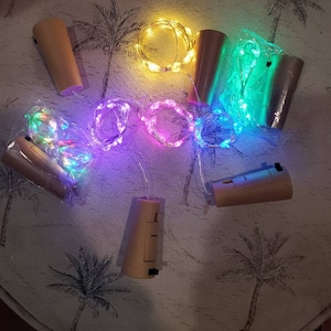 May include: A collection of cork-shaped LED string lights in various colors, including yellow, green, purple, and multi-color. The lights are designed to fit inside bottles, creating a decorative lighting effect. The corks have an on/off switch.