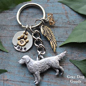 Könnte beinhalten: Silberner Schlüsselanhänger mit einem silbernen Hundefiguren-Anhänger, einem goldenen Pfotenabdruck-Anhänger mit einem Herz, einem goldenen Engelsflügel-Anhänger und einem silbernen Anhänger mit dem eingravierten Namen "Jake".