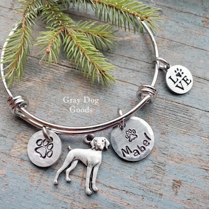 May include: A silver charm bracelet with a dog paw print charm, a charm with the word "LOVE" on it, a charm with a dog silhouette, and a charm with the name "Mabel" on it.