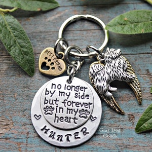 May include: Silver keyring with a round charm that reads "no longer by my side but forever in my heart" and a smaller charm with the name "HUNTER". The keyring also features a small heart charm with the words "BEST FRIEND" and a paw print, and a charm of a dog with angel wings.