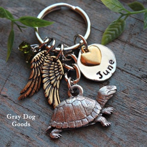 May include: A silver turtle charm keychain with a gold heart charm, angel wings, and a green crystal charm. The keychain has a silver tag with the name "June" engraved on it.