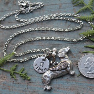 May include: Silver necklace with a charm of a dachshund with wings, a paw print charm, and a personalized tag that says "Piper".