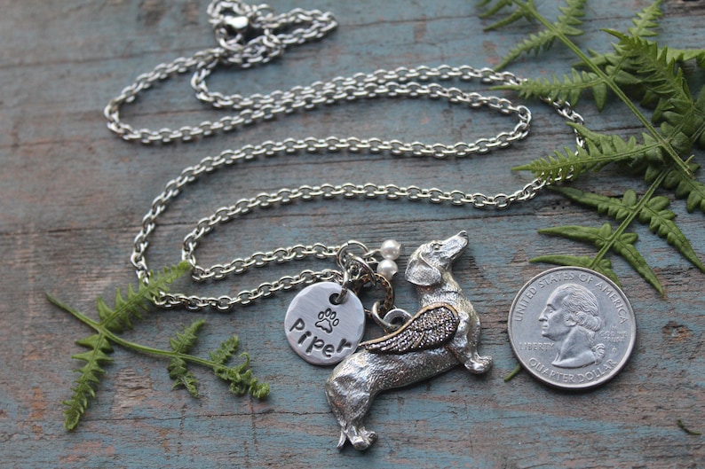 May include: Silver necklace with a charm of a dachshund with wings, a paw print charm, and a personalized tag that says "Piper".
