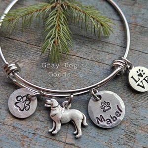 May include: A silver expandable bracelet with charms. The charms include a paw print, a dog silhouette, and two round charms with paw prints and the text "LOVE" and "Mabel".