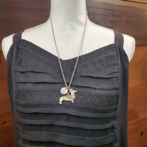 May include: A silver chain necklace with a small silver charm and a dachshund charm. The necklace is on a black dress form.