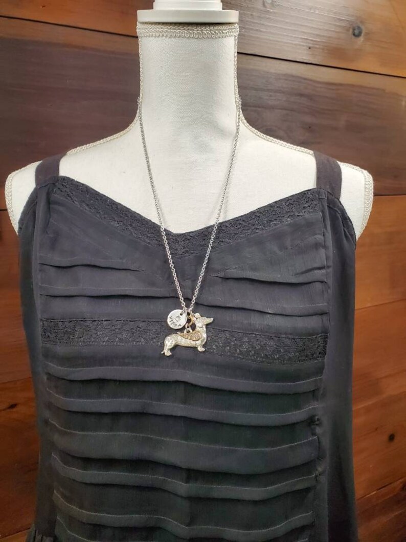 May include: A silver chain necklace with a small silver charm and a dachshund charm. The necklace is on a black dress form.