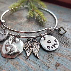 K&ouml;nnte beinhalten: Silbernes Armband mit einem Hasen-, Fl&uuml;gel-, Herz- und einem Anh&auml;nger mit dem eingravierten Namen "Piper".