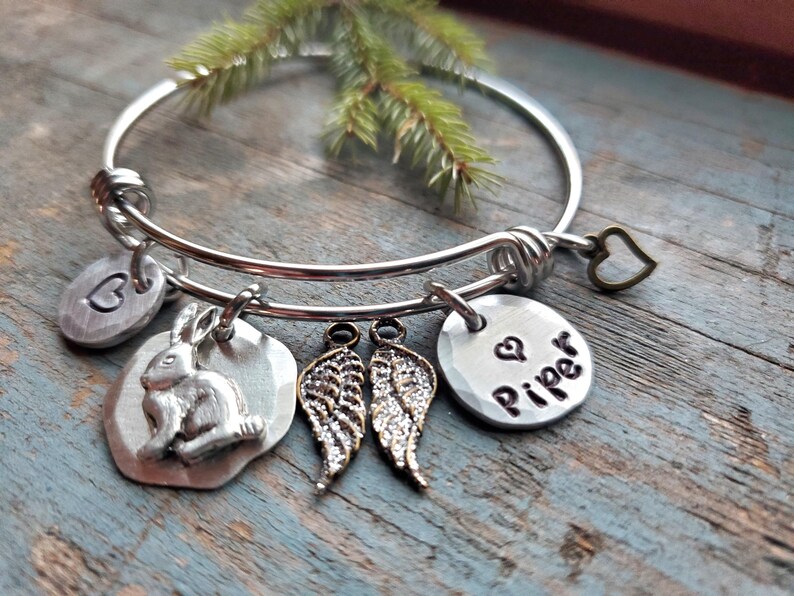K&ouml;nnte beinhalten: Silbernes Armband mit einem Hasen-, Fl&uuml;gel-, Herz- und einem Anh&auml;nger mit dem eingravierten Namen "Piper".