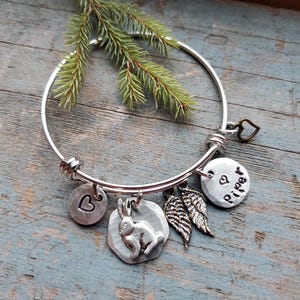 K&ouml;nnte beinhalten: Silbernes Armband mit einem Hasen-Anh&auml;nger, einem Herz-Anh&auml;nger, einem Fl&uuml;gel-Anh&auml;nger und einem Anh&auml;nger mit dem Namen "Piper" darauf.