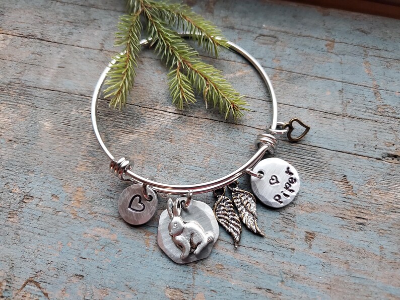 K&ouml;nnte beinhalten: Silbernes Armband mit einem Hasen-Anh&auml;nger, einem Herz-Anh&auml;nger, einem Fl&uuml;gel-Anh&auml;nger und einem Anh&auml;nger mit dem Namen "Piper" darauf.