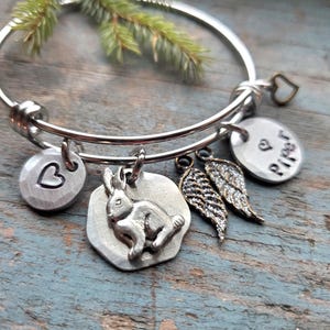 K&ouml;nnte beinhalten: Ein silbernes, ausziehbares Armband mit mehreren Anh&auml;ngern. Die Anh&auml;nger umfassen ein Herz, ein Kaninchen, ein Paar Engelsfl&uuml;gel und einen Anh&auml;nger mit dem Wort "Piper" darauf.