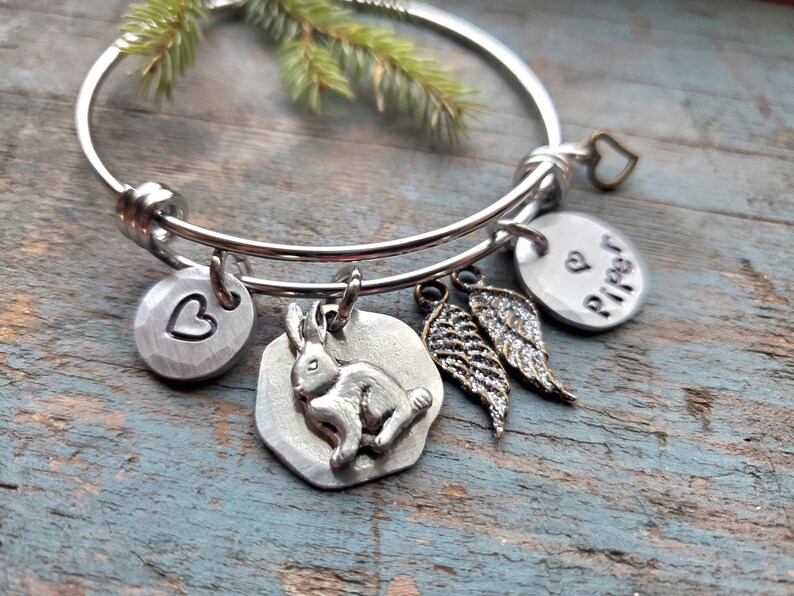 K&ouml;nnte beinhalten: Ein silbernes, ausziehbares Armband mit mehreren Anh&auml;ngern. Die Anh&auml;nger umfassen ein Herz, ein Kaninchen, ein Paar Engelsfl&uuml;gel und einen Anh&auml;nger mit dem Wort "Piper" darauf.