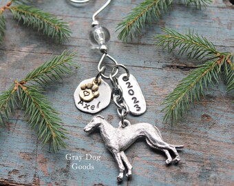 May include: Silver and gold Christmas ornament featuring a greyhound dog, a paw print charm with a heart, and a tag that says "Axel" and "2023".