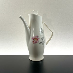 May include: White ceramic coffee pot with a floral design featuring a pink rose and gray leaves. The pot has a lid and a handle.