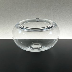 Puede incluir: Un cuenco de vidrio transparente con forma redondeada. El cuenco está sobre una superficie negra.