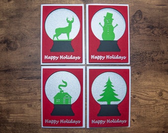 May include: Four red Christmas cards with silver glitter snow globes. Each card features a different holiday image: a deer, a snowman, a house, and a Christmas tree. The cards all say "Happy Holidays".