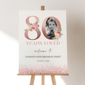 Può includere: Un cartello di benvenuto per una festa di 80 anni. Il cartello presenta una foto di un bambino, le parole "80 anni amati" e il nome "Connie". Il cartello è decorato con elementi floreali e glitter.