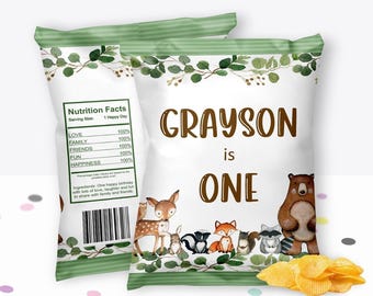 May include: Two white chip bags with a green leafy border and the text "GRAYSON is ONE". The bags feature woodland animal illustrations and a "Nutrition Facts" label. A small pile of chips is in front of the bags.