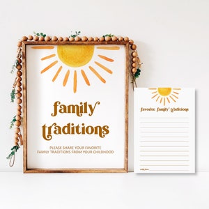 A wooden-framed printable sign featuring a retro watercolor half-sun in orange and yellow, reading "family traditions" with instructions "PLEASE SHARE YOUR FAVORITE FAMILY TRADITIONS FROM YOUR CHILDHOOD". Beside the frame sits a matching printable card titled "favorite family traditions" with lined spaces for guest notes.