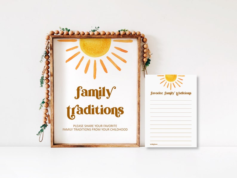 A wooden-framed printable sign featuring a retro watercolor half-sun in orange and yellow, reading "family traditions" with instructions "PLEASE SHARE YOUR FAVORITE FAMILY TRADITIONS FROM YOUR CHILDHOOD". Beside the frame sits a matching printable card titled "favorite family traditions" with lined spaces for guest notes.