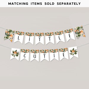 May include: A white banner with orange blossom and fruit designs. The banner spells out "Little Cutie" in black letters.