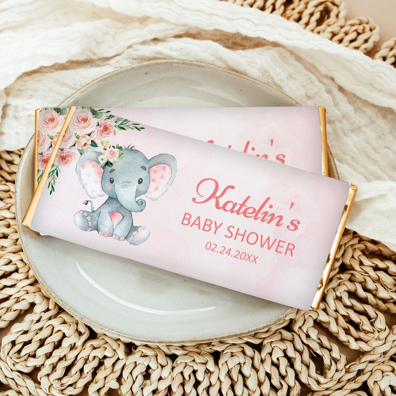 May include: Pink and white baby shower chocolate bar wrapper featuring a grey elephant illustration wearing a pink flower crown. The wrapper has gold foil accents and the text "Katelyn's Baby Shower 02.24.20XX".